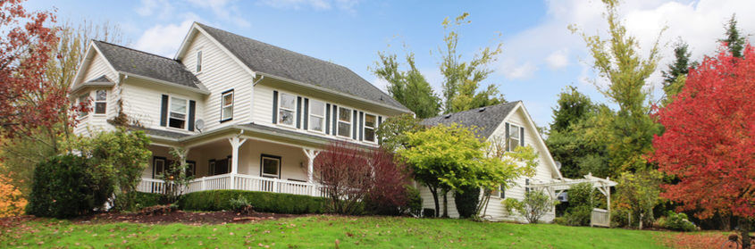 Two-story white farmhouse with a wraparound porch surrounded by autumn trees
